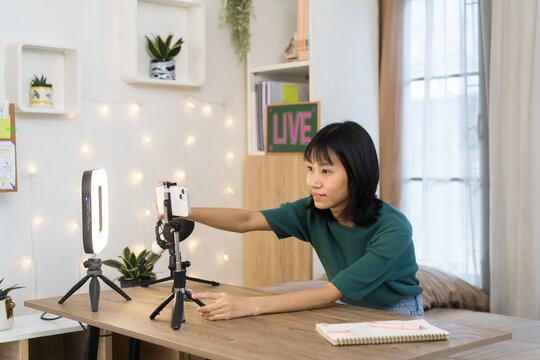 Young woman prepares adjusting smartphone on table for a live broadcast in home studio
