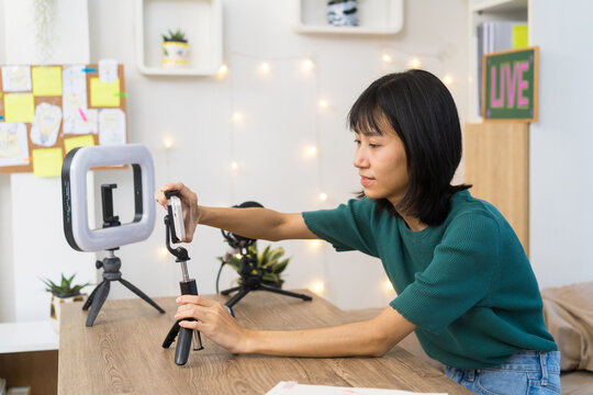 Young content creator carefully adjusts her smartphone on a tripod in a home studio for Video Recording