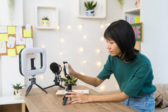 Young content creator carefully adjusts her smartphone on a tripod in a home studio for Video Recording
