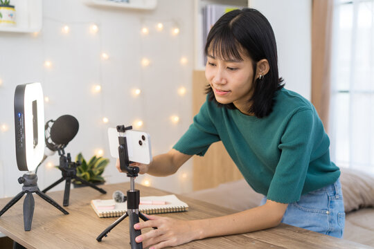 Young content creator carefully adjusts smartphone on a tripod and Ring Light in a home studio for Video Recording