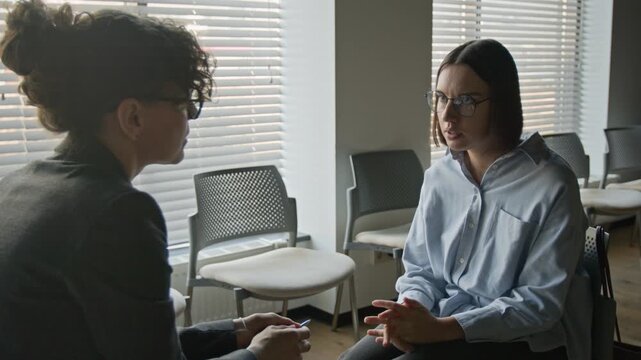 Zoom in shot of Caucasian young woman with glasses talking to female psychotherapist during counseling session. Clip for mental health awareness campaigns and therapy service advertisements