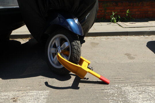 A wheel lock is attached to a scooter, preventing the motorcycle from moving. Illegal parking on the side of the road, violating parking rules.