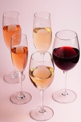 Fototapeta premium Assorted wine and champagne glasses with sparkling rose white and red wine. Drinks stand on pink background. Elegant variety of bubbly beverages for festive celebrations.