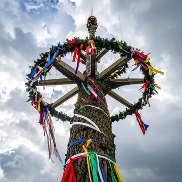 A wooden pole adorned with colorful ribbons and greenery under a cloudy sky