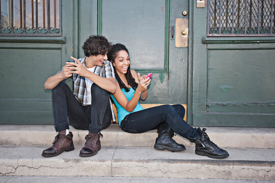 Couple using cell phones on front stoop