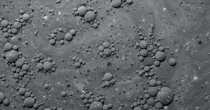 Black bubbly liquid rotation. Close-up of dark viscous surface with dense foam and bubbles. Smooth continuous rotation reveals shifting patterns and light reflections.