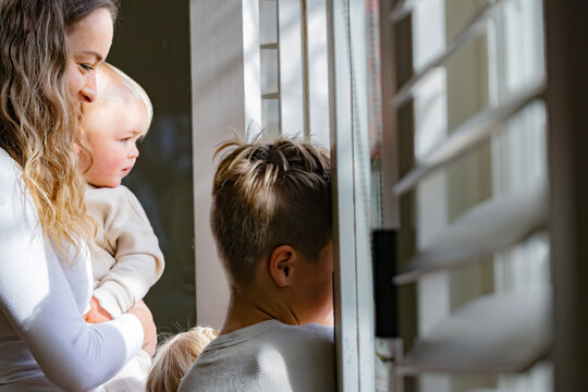 Mother carrying baby looking through an open door with other brothers nearby