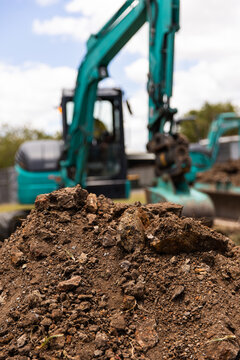 Close-up view of freshly dug soil in the foreground with a teal excavator in the background