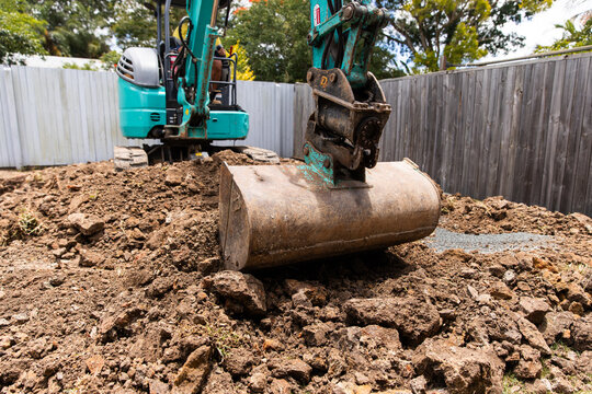 Excavator positioned on a mound of soil and rocks with bucket lowered down