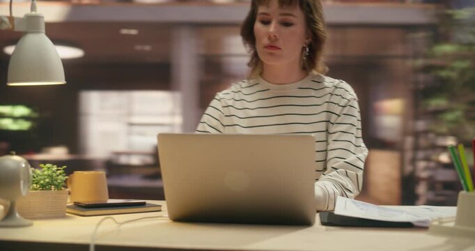360 Degree. Caucasian Woman Compares Financial Charts on Laptop Computer With Statistics Documents in Office, Optimising Workflow and Productivity at Desk. Orbital Cinematic Arc Tracking Shot.