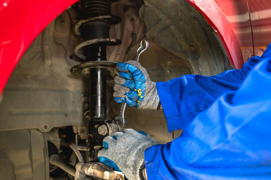 Close up unrecognized car mechanic working on vehicle suspension system, repairing and assembling a coil spring onto a shock absorber strut inside auto repair shop garage