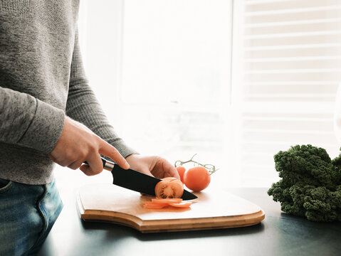 Preparing fresh vegetables with knife on wooden cutting board