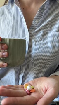 Woman keeping in hand different colorful pills and tablets with cup of water close up. Taking daily dose of vitamins and supplements, home treatment, woman's health, medicine and biohacking.