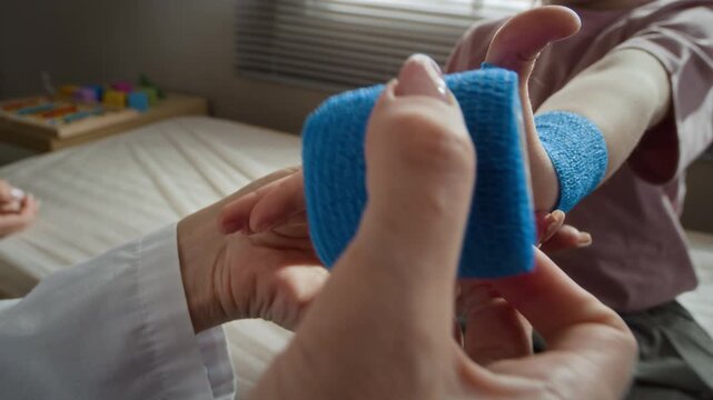 Closeup of female pediatrician wrapping blue elastic bandage around child patient wrist in clinic. Clip is ideal for pediatric clinic promotions and medical insurance advertising