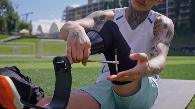 Man athlete screws bionic prosthetic leg with spanner on lawn