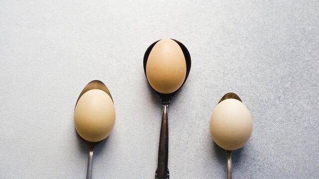 Three eggs resting on spoons on a grey surface
