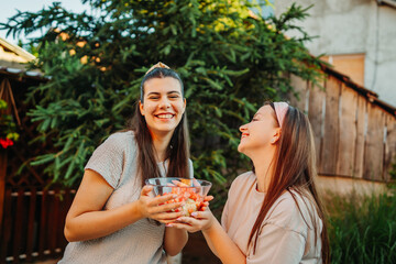 Fototapeta premium Young women sharing fruit salad, enjoying healthy summer friendship