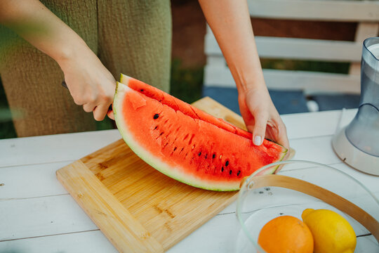 Woman slicing fresh watermelon on cutting board outdoors