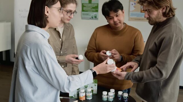 Zoom out shot of diverse group of young adults examining and discussing dietary supplement bottles during wellness workshop. Clip for healthcare marketing and vitamin product promotions