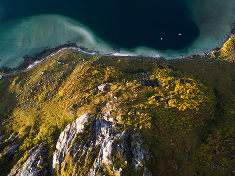 Aerial view of the rocky mountain peak and autumn foliage overlooking a turquoise bay and sandy beach in Leknes, Nordland, Norway.