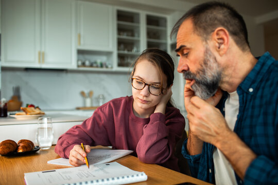 Parent helping teen with homework at kitchen table at home