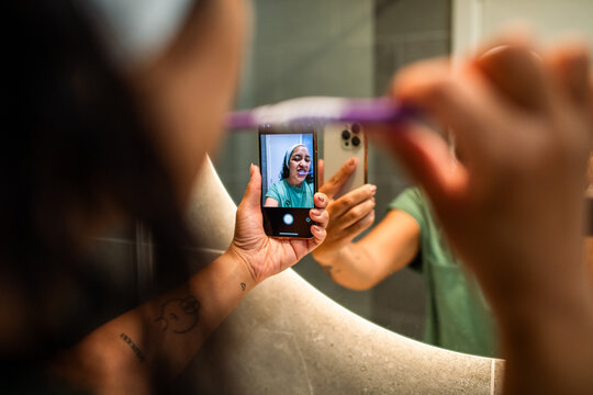 Woman brushing teeth taking mirror selfie in bathroom