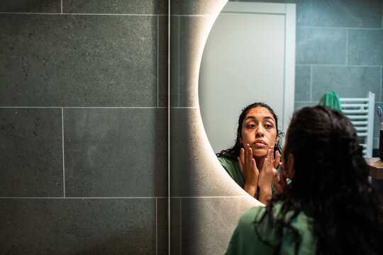 Woman examining face in home bathroom mirror