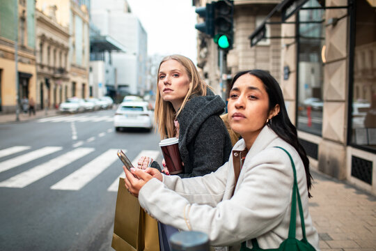 Two women wait at urban crosswalk with shopping bags