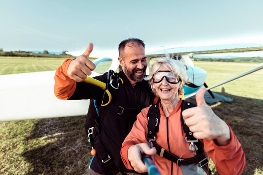 Senior woman and instructor taking selfie with thumbs up after skydiving at airfield