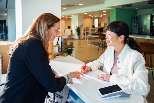 Businesswomen signing contract at reception desk in modern office