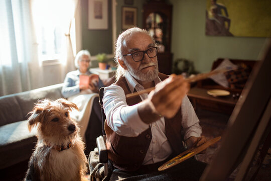 Senior man painting at home with dog nearby