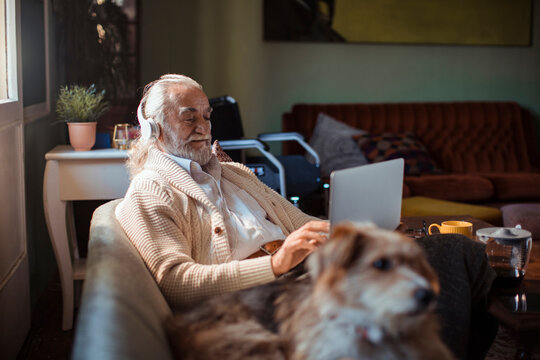 Senior man with headphones using laptop in cozy living room