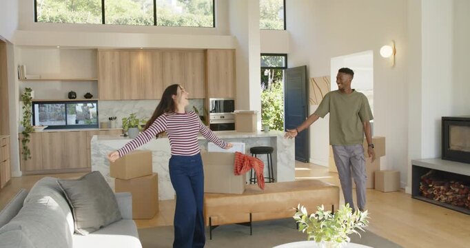 Couple moving into new home, woman spinning toward African American man by stacked moving boxes