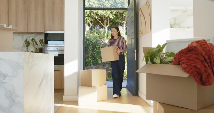 Woman entering through door carrying box, stacking and adjusting top box at entry while unpacking