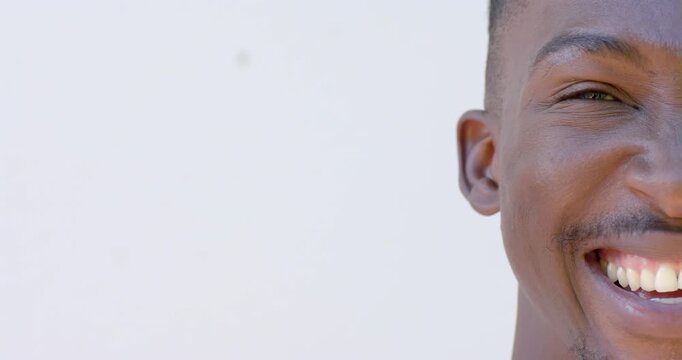 Man reacting to camera prompt, smiling, opening eye against white wall, copy space