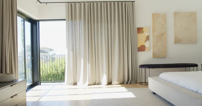 Full-height beige curtain is swaying as open balcony door is letting breeze and sun fill room