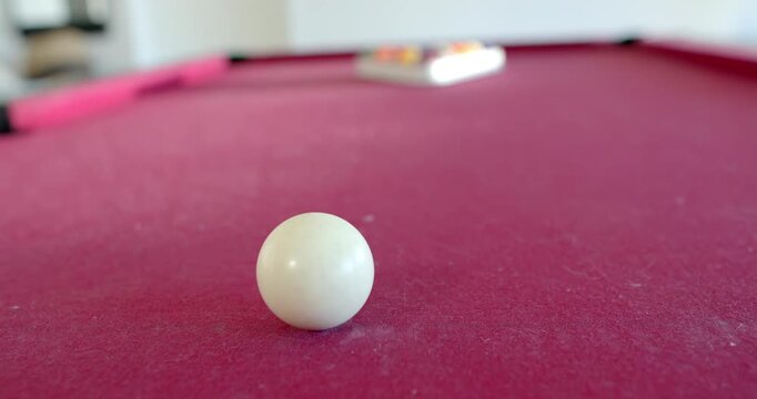 White cue ball is rolling toward camera after tap, slowing into rest on pink felt table