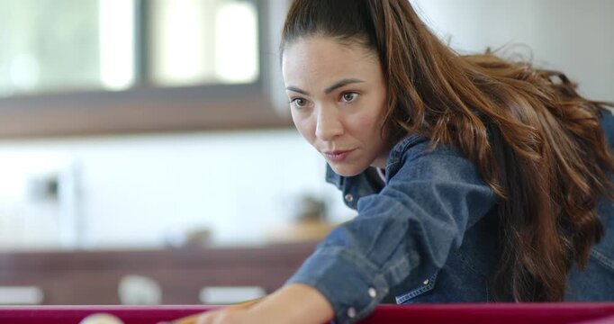 Adult woman aiming to pocket ball, leaning on red-felt pool table, aligning cue, striking cue ball