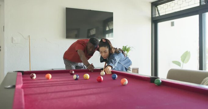 Couple man leaning and pointing, guiding woman lining up shot on magenta pool table watching balls