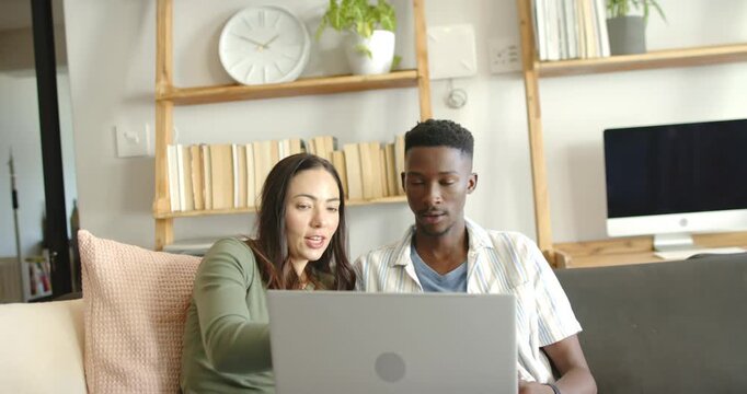 Couple sitting on couch at home, woman leaning pointing at laptop reviewing content, man nodding