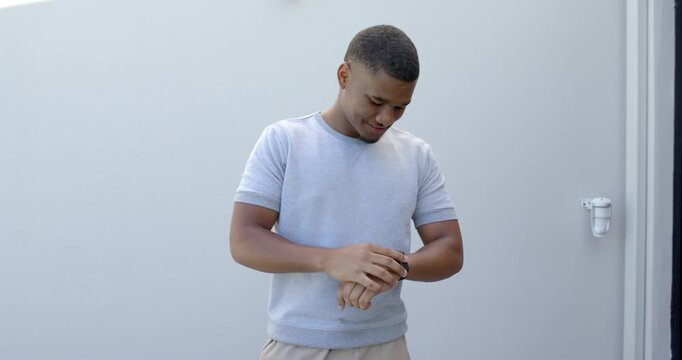 African American man checking smartwatch after alert, tapping, glancing up and smiling by gray wall