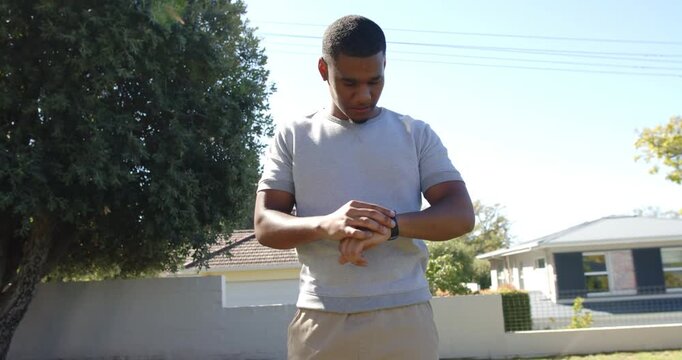 African American man adjusting smartwatch, shifting gaze, smiling, responding in front yard