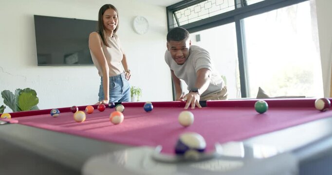 African American couple playing pool in living room, woman encouraging man aiming with cue stick
