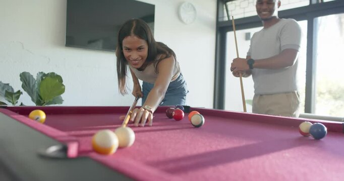 African American couple, man smiling, urging woman aiming, striking, laughing at magenta-felt table