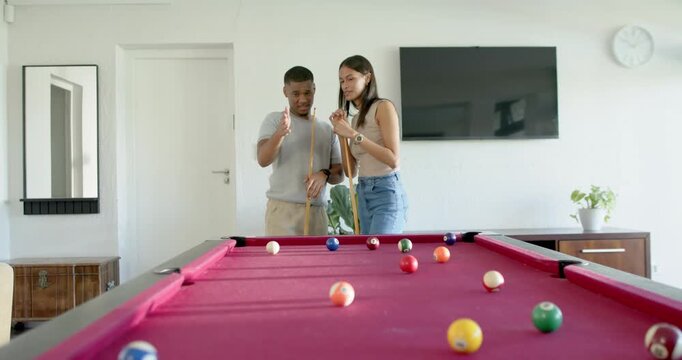 Couple standing behind red-felt pool table at home, seeing balls, planning shot and aligning cues