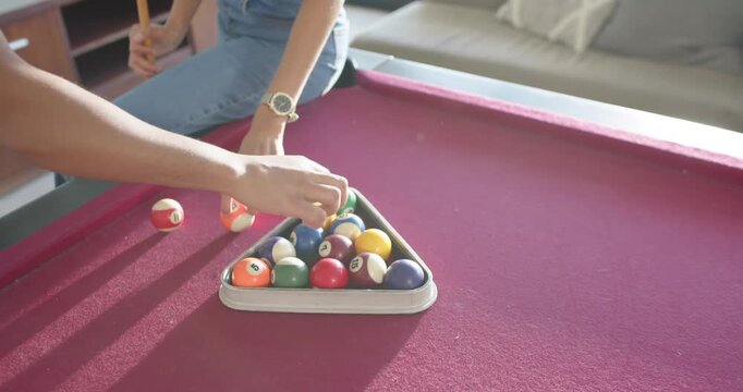 African American couple holding rack, placing orange ball and racking balls at home preparing game