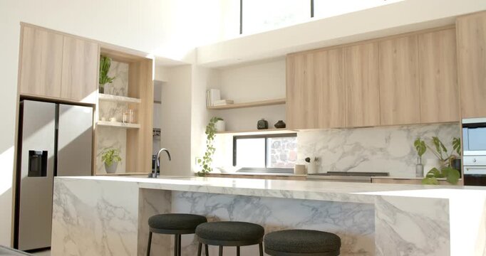 Camera is sweeping across marble kitchen island with three black stools to showcase cabinets