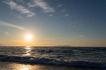 Obraz premium Golden sunset over ocean horizon with sea foam and distant island