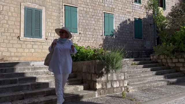 Senior Woman Walking Down Steps in Mediterranean Old Town. Senior female tourist walking down stone steps in a historic Mediterranean old town. Active retirement, independent travel and sightseeing.