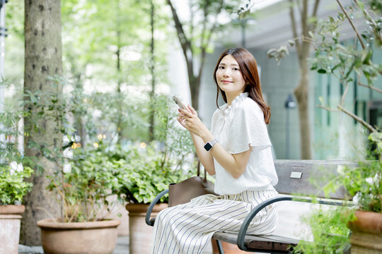 ベンチでスマートフォンを使う日本人女性のリラックスタイム